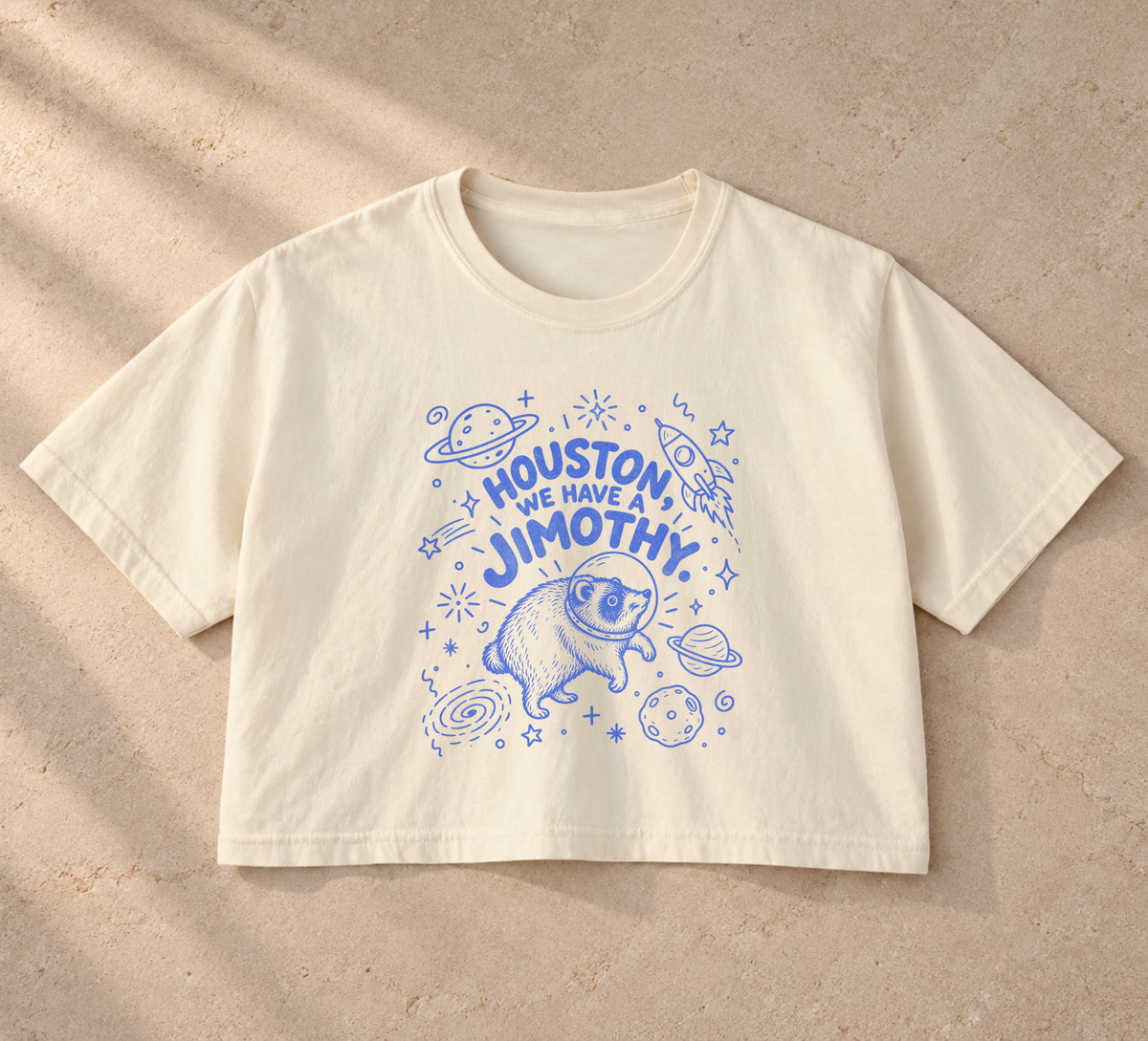 Women’s Comfort Colors Ivory boxy tee with blue “Houston, We Have a Jimothy” lettering and a raccoon astronaut surrounded by planets, stars, and a rocket.